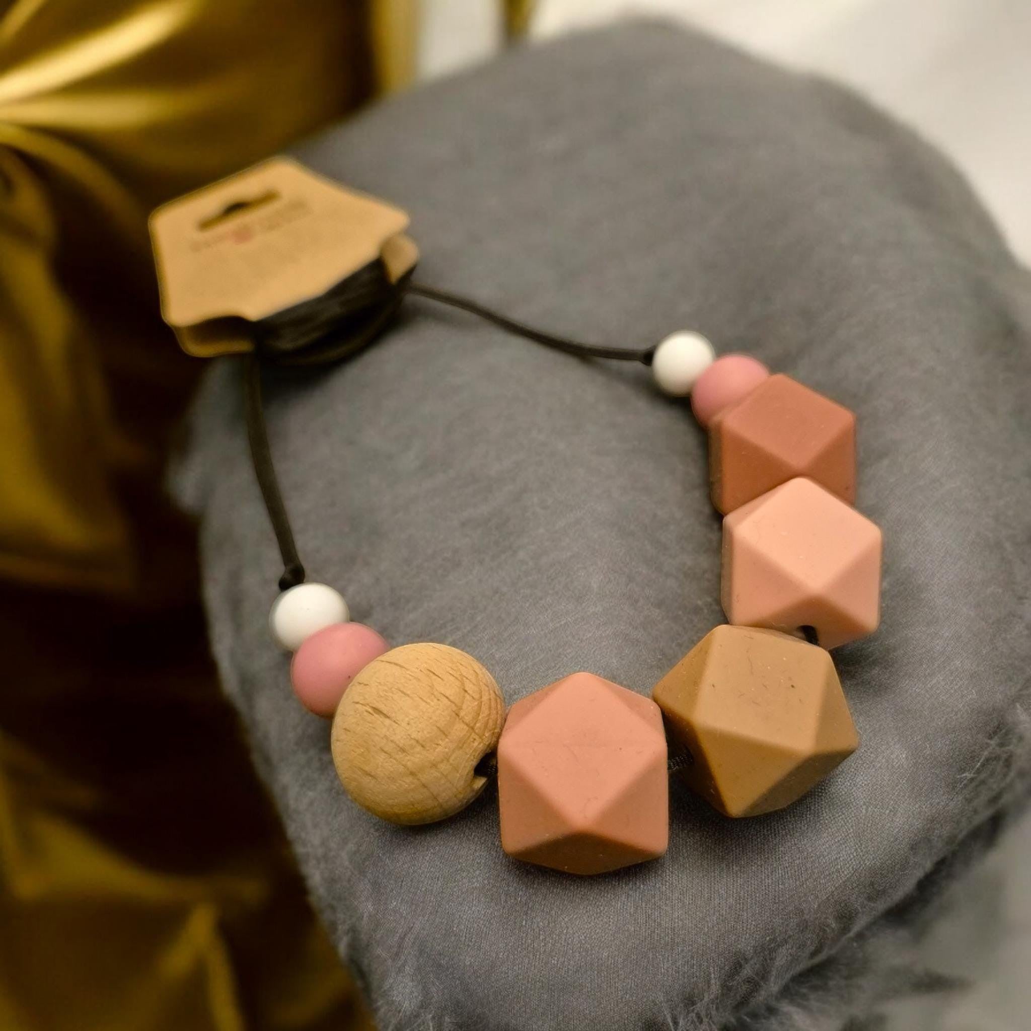 Precious Days Gifts chunky neutral silicone and wood teething necklace for babies. Features geometric and round beads in pink, beige, and white.