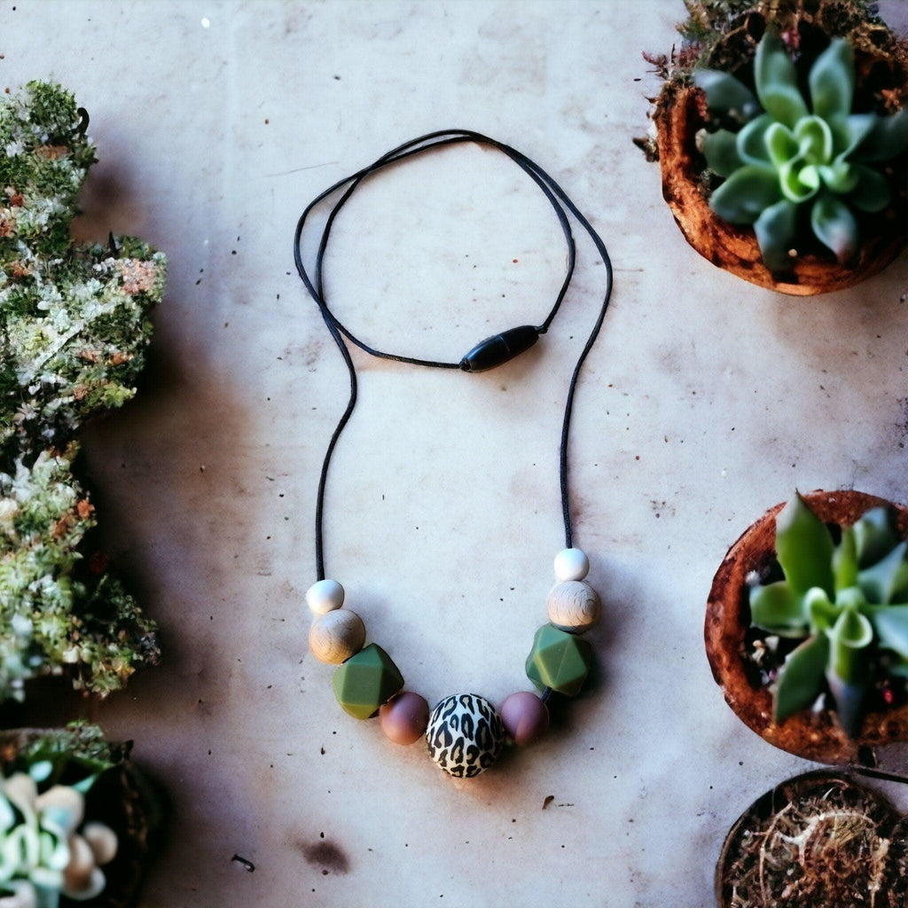Precious Days Gifts earthy animal print teething necklace with silicone and wood beads in green, pink, and white.