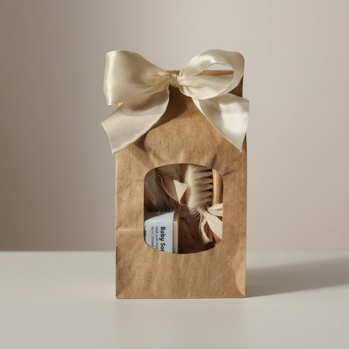 Precious Days Gifts baby bath essentials gift set in a brown paper bag with a cream ribbon bow. Includes washcloths, soap, and a brush and comb.