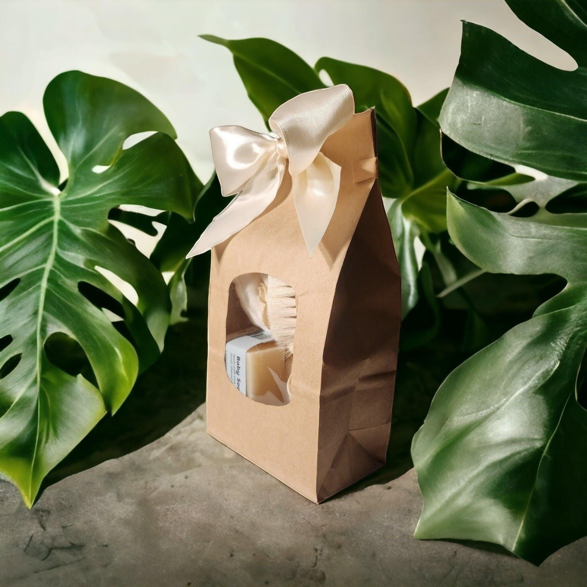 Precious Days Gifts baby bath essentials gift set in a brown paper bag with a cream bow, containing soap and a brush.