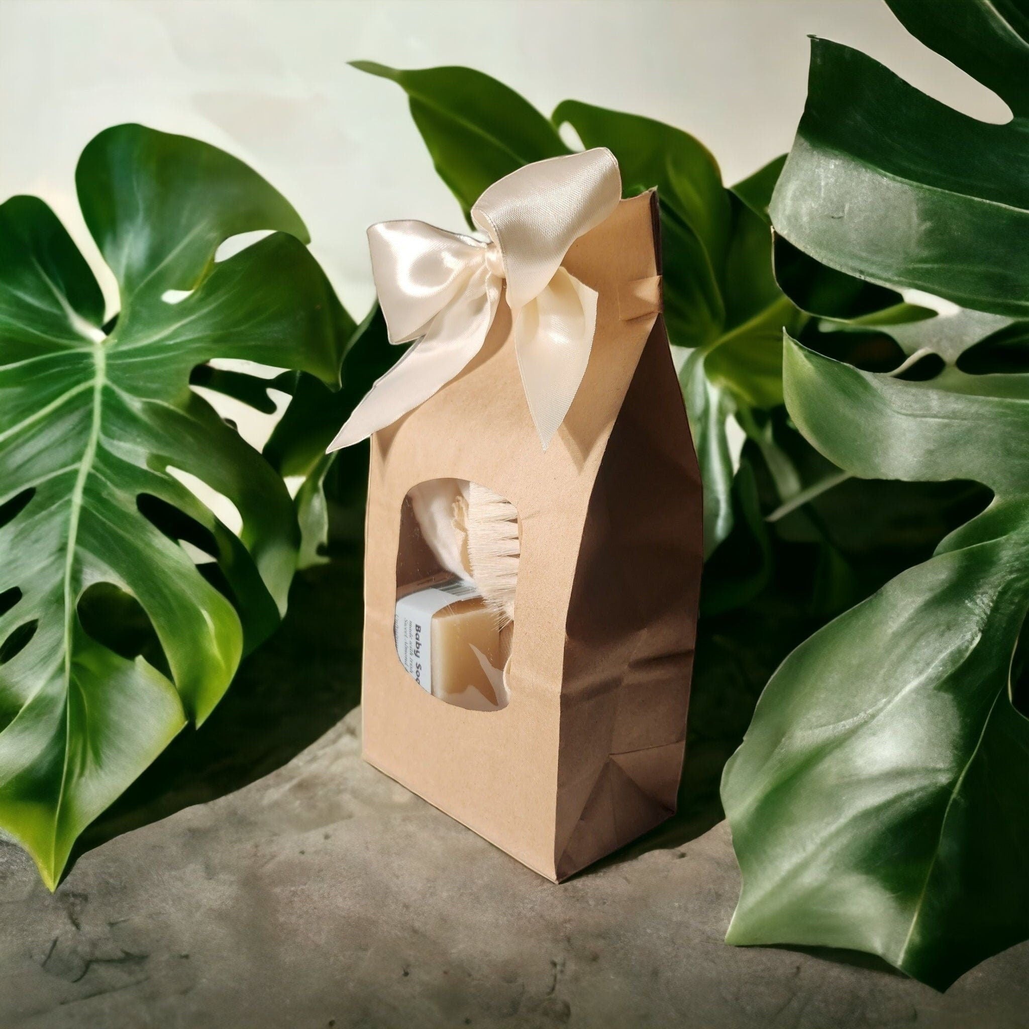 Precious Days Gifts baby bath gift set in a brown paper bag with a cream ribbon, containing soap and a brush.