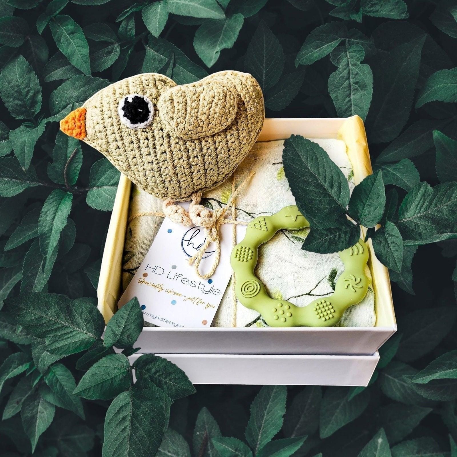Precious Days Gifts new baby gift box with a beige crochet bird rattle, green silicone teether, and patterned muslin.