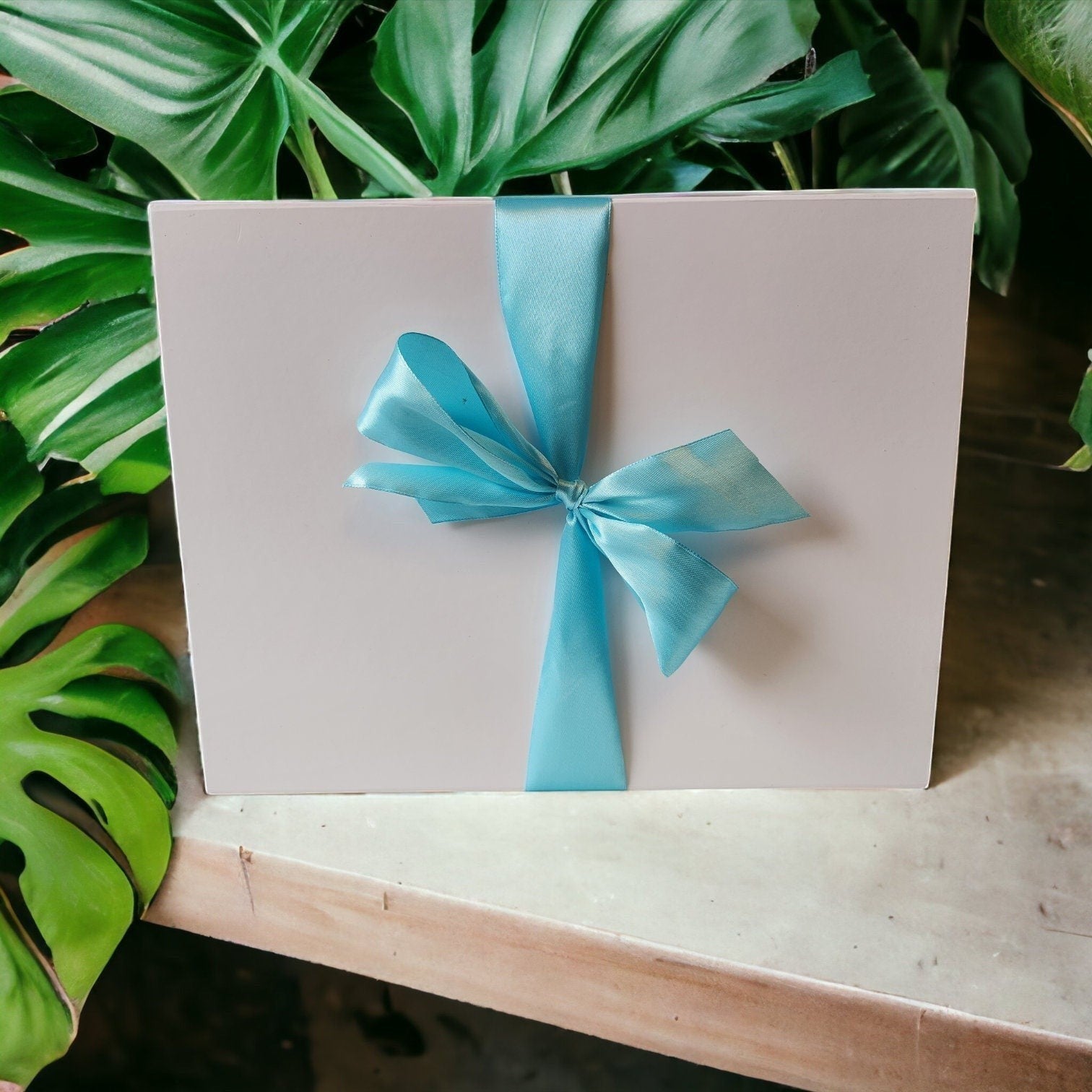 Precious Days Gifts large new baby gift box with blue ribbon and bow, surrounded by green leaves.