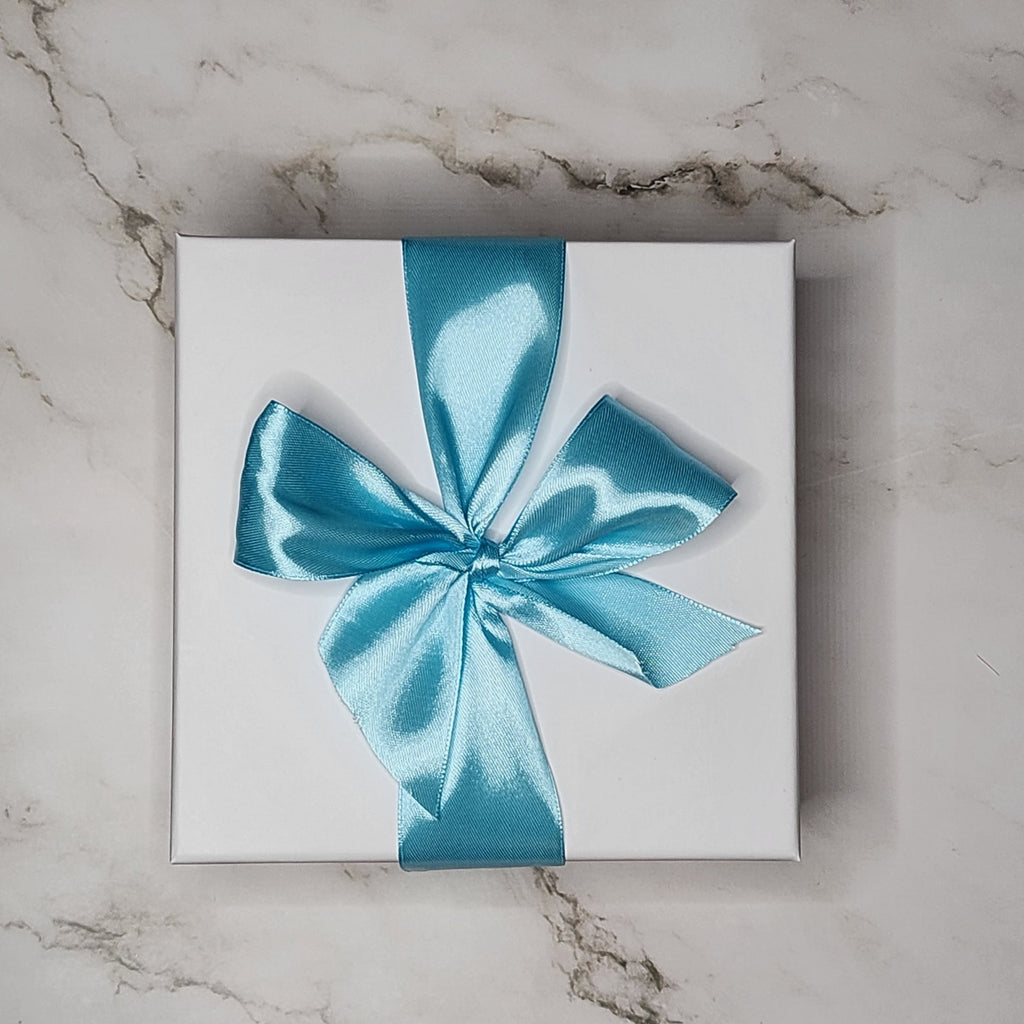 Precious Days Gifts small baby gift box with a blue satin ribbon bow, presented on a marble surface.