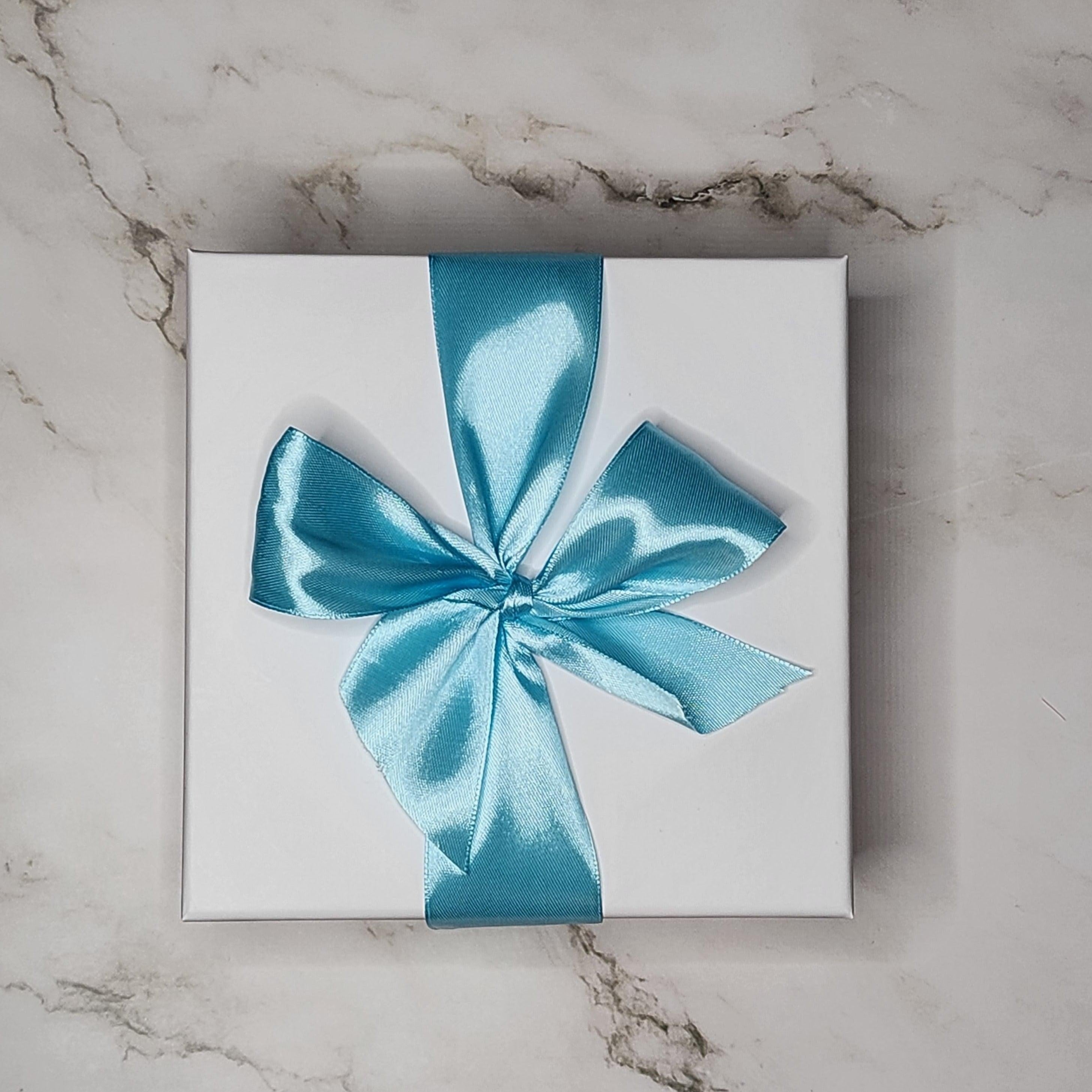 Precious Days Gifts Small New Baby Gift Box with rainbow muslin, rattle, and teether, tied with a blue ribbon.
