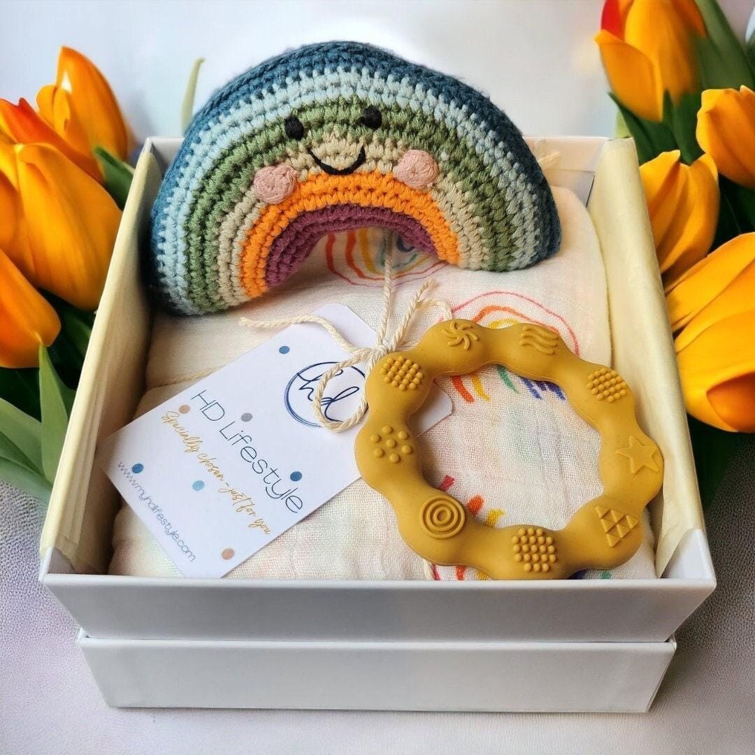 Precious Days Gifts new baby gift box with a crochet rainbow rattle, yellow silicone teether, and rainbow print muslin.