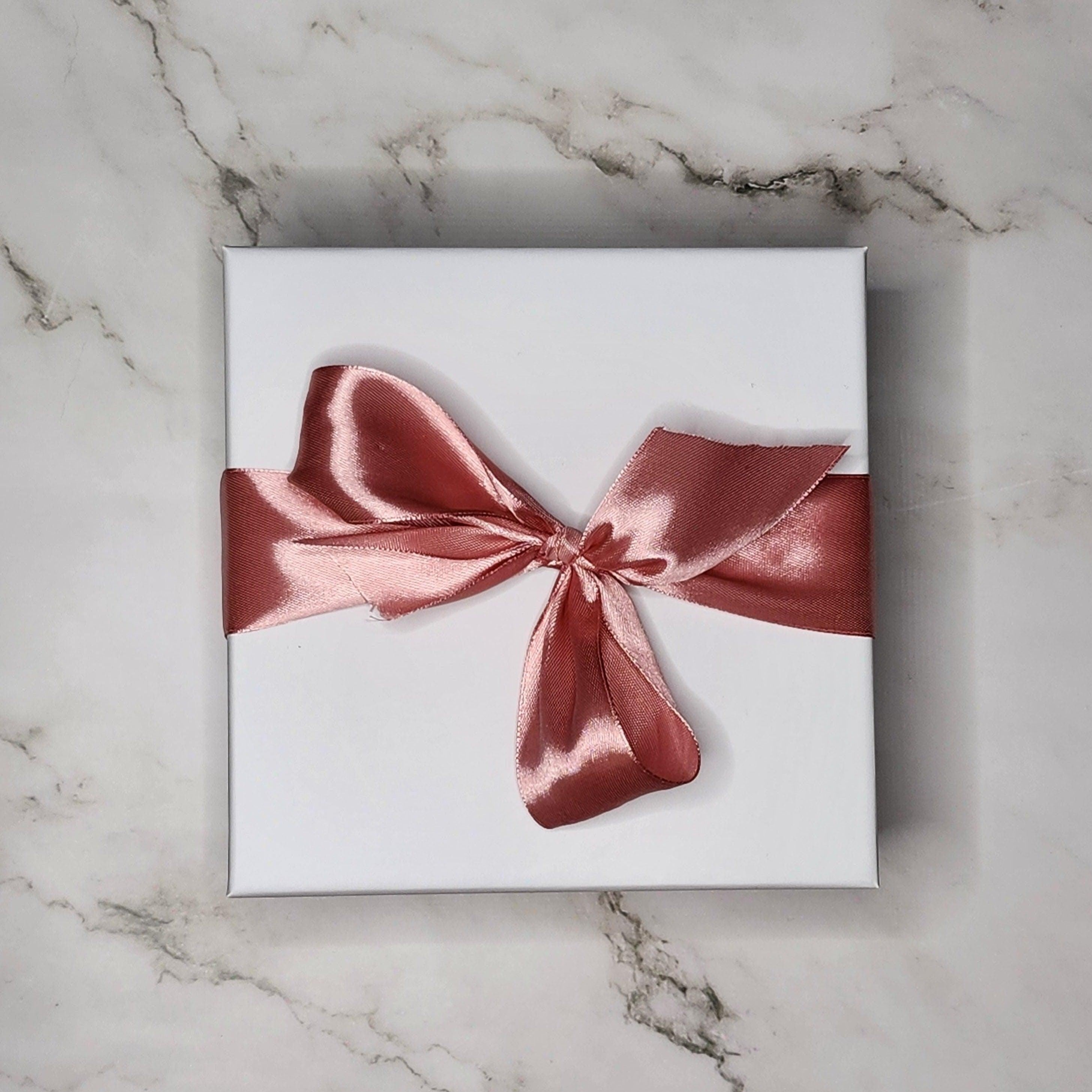 Precious Days Gifts white gift box with rose gold ribbon bow, containing new baby items.