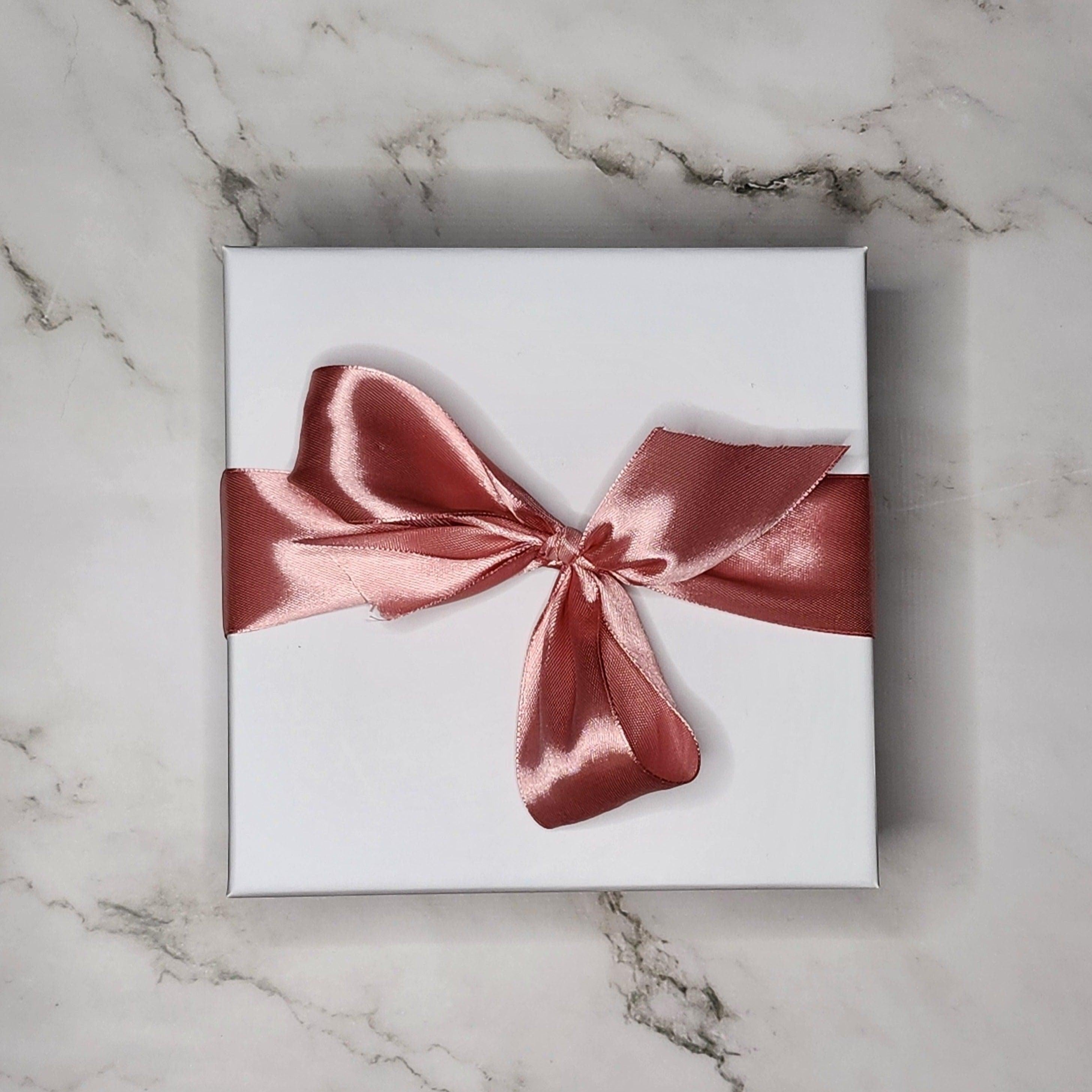 Precious Days Gifts white gift box with rose gold ribbon bow, containing baby muslin, bird rattle, and teether.