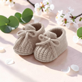 Precious Days Gifts beige knitted baby booties with a soft cable-knit texture and decorative front bow detail.