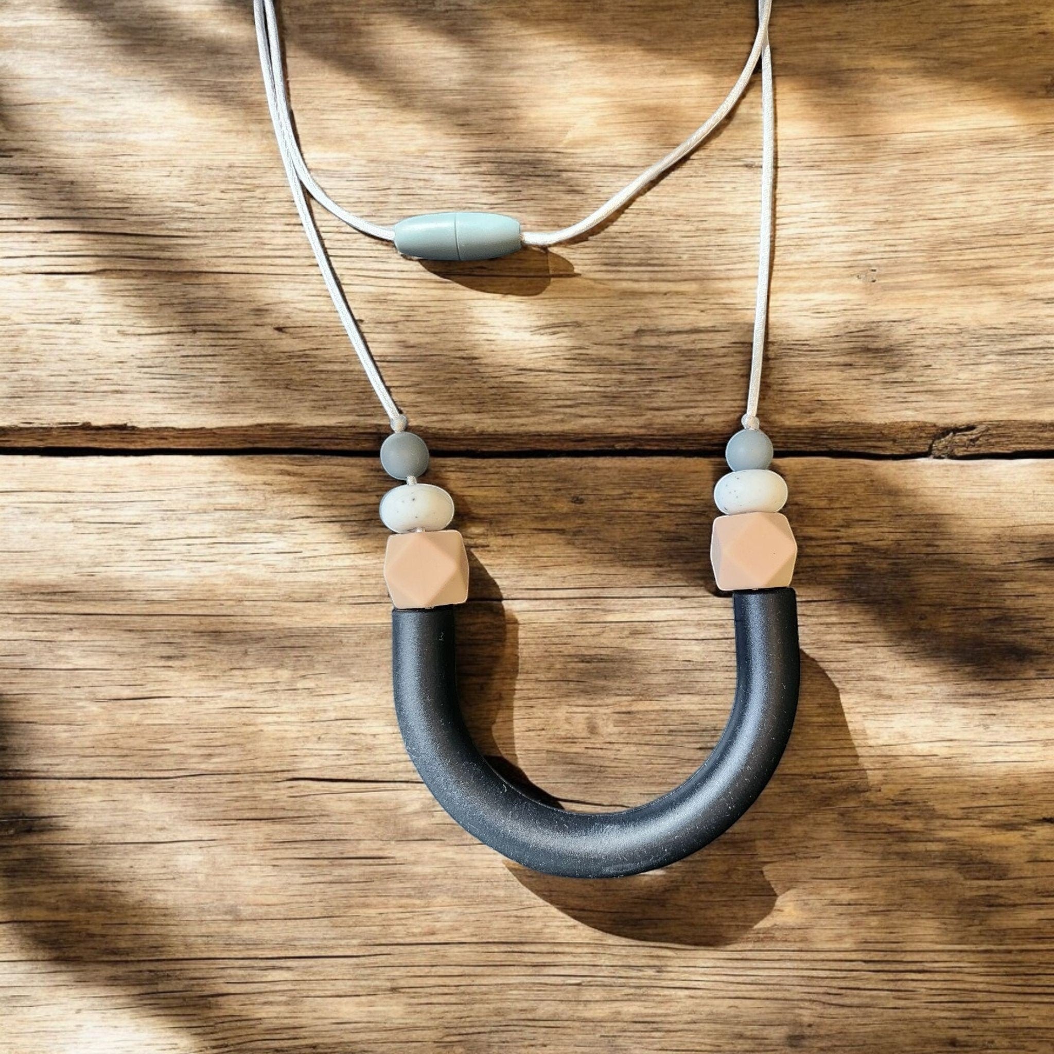 Precious Days Gifts black silicone U-shape teething necklace with grey, white speckled, and peach hexagon beads.