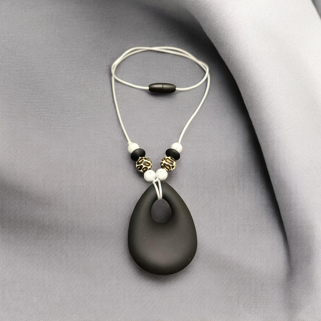 Precious Days Gifts black teardrop silicone teething necklace with leopard print and white beads on a white cord.