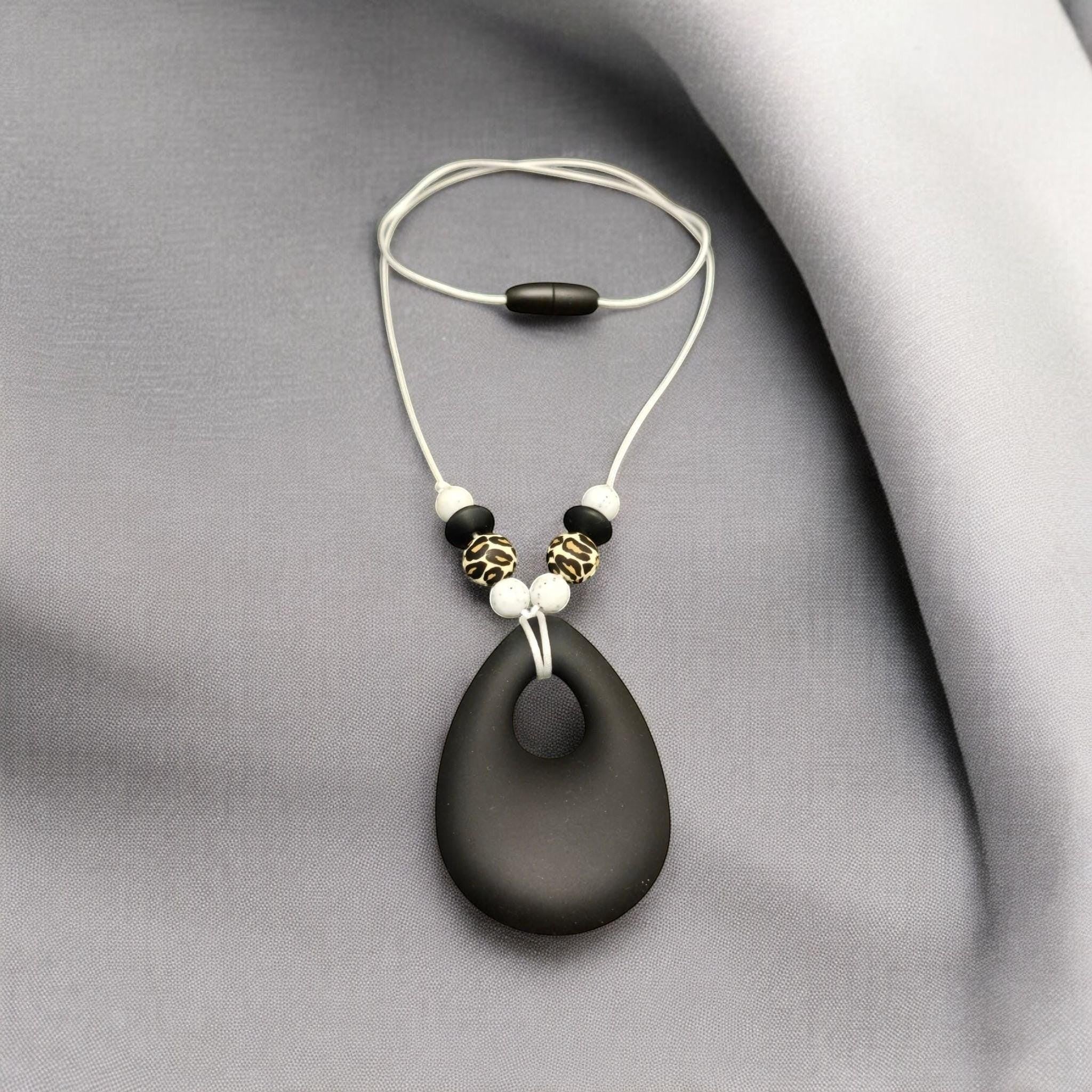 Precious Days Gifts black teardrop silicone teething necklace with leopard print and white beads on a white cord.