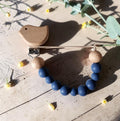 Precious Days Gifts blue bird dummy clip with natural wooden beads and smooth silicone on a rustic wooden surface.