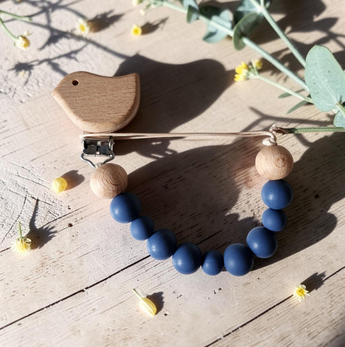 Precious Days Gifts blue bird dummy clip with natural wooden beads and smooth silicone on a rustic wooden surface.