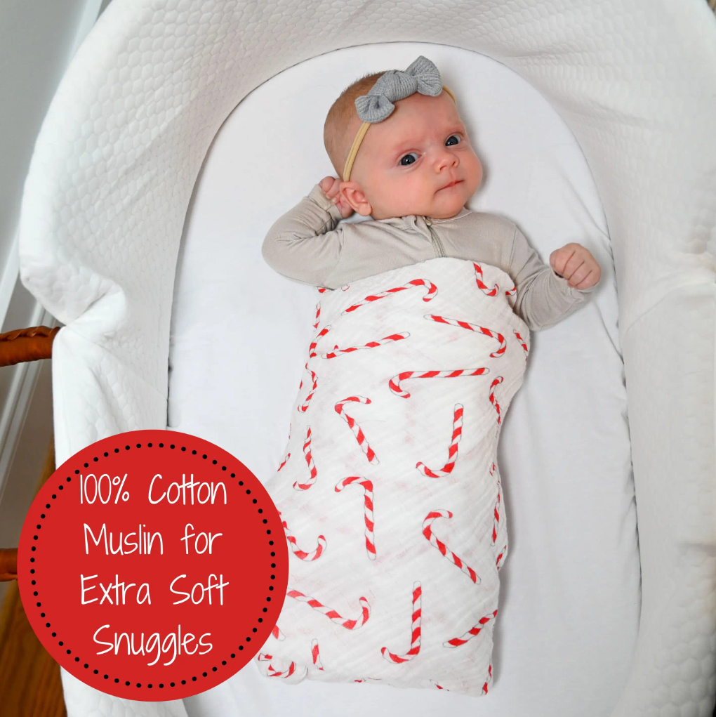 Precious Days Gifts baby swaddled in a white muslin blanket with a festive red and white candy cane print in a bassinet