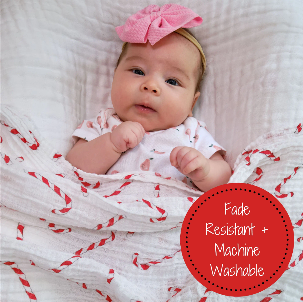 Precious Days Gifts baby wrapped in a white muslin swaddle blanket with a festive red and white candy cane print.