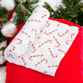 Precious Days Gifts white cotton muslin swaddle blanket with a festive red candy cane print for the holidays