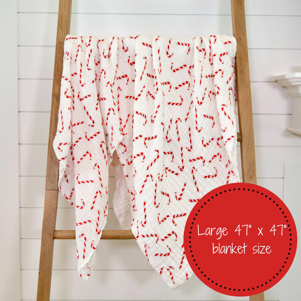 Precious Days Gifts white muslin baby swaddle blanket with a festive red candy cane pattern draped on a wooden ladder