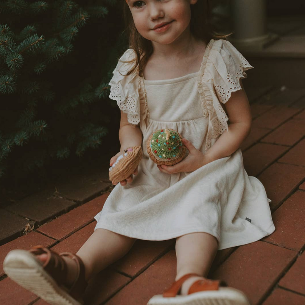 Young girl sitting on a brick porch holding Precious Days Gifts organic cotton Christmas sugar cookie and cupcake rattles