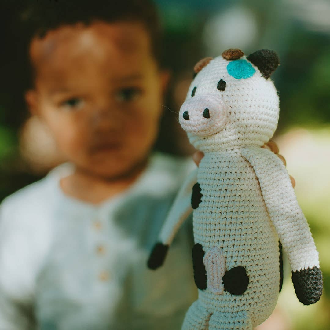 Precious Days Gifts handmade organic cotton crochet cow plush toy with black spots and blue accent.