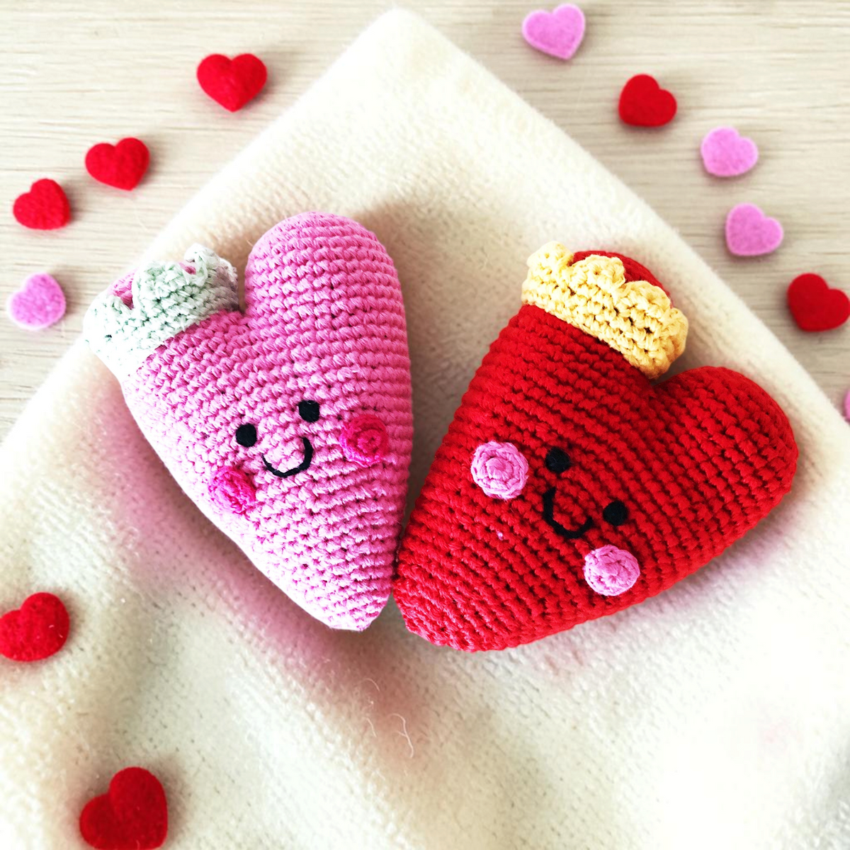 Precious Days Gifts crochet heart rattles in pink and red with cute faces and crowns on a soft cream blanket