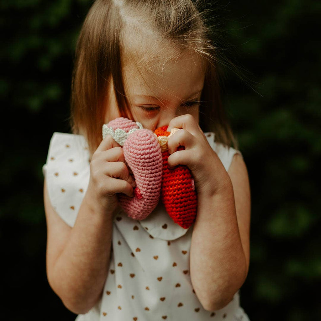 Precious Days Gifts crochet heart rattles in pink and red held by a young girl in a heart-patterned dress