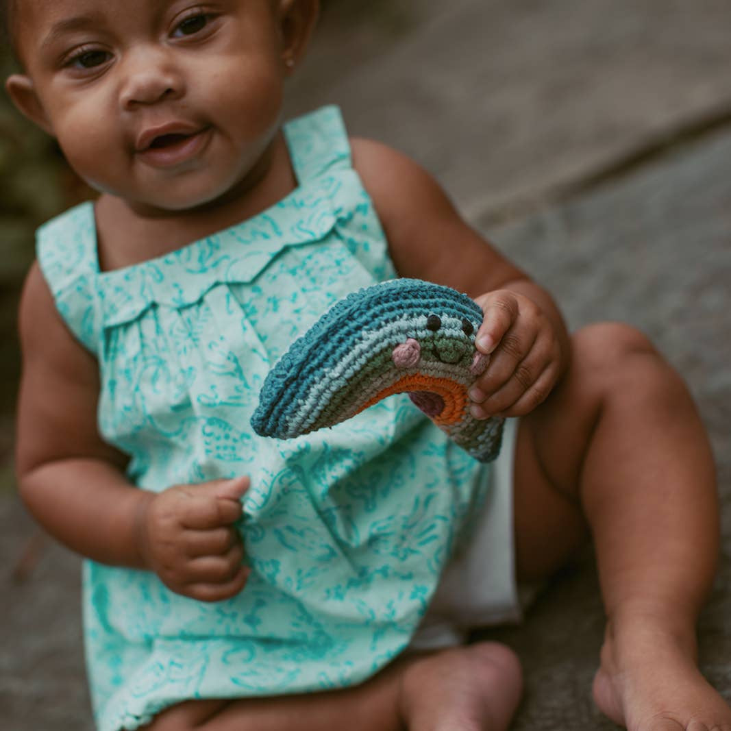 Precious Days Gifts handmade cotton boho rainbow rattle held by a baby in a mint green patterned dress