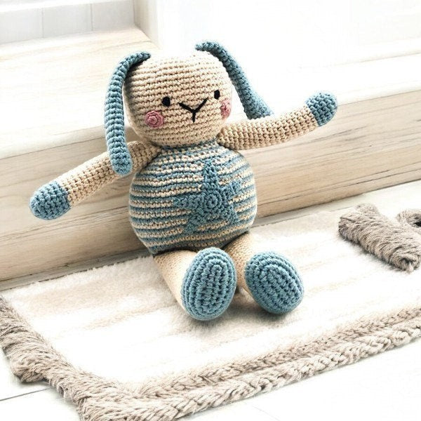 Precious Days Gifts crocheted bunny toy with blue stripes and ears, sitting on a cream rug.