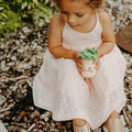 Precious Days Gifts crocheted pineapple rattle toy with green leaves and a smiling face, held by a young girl.