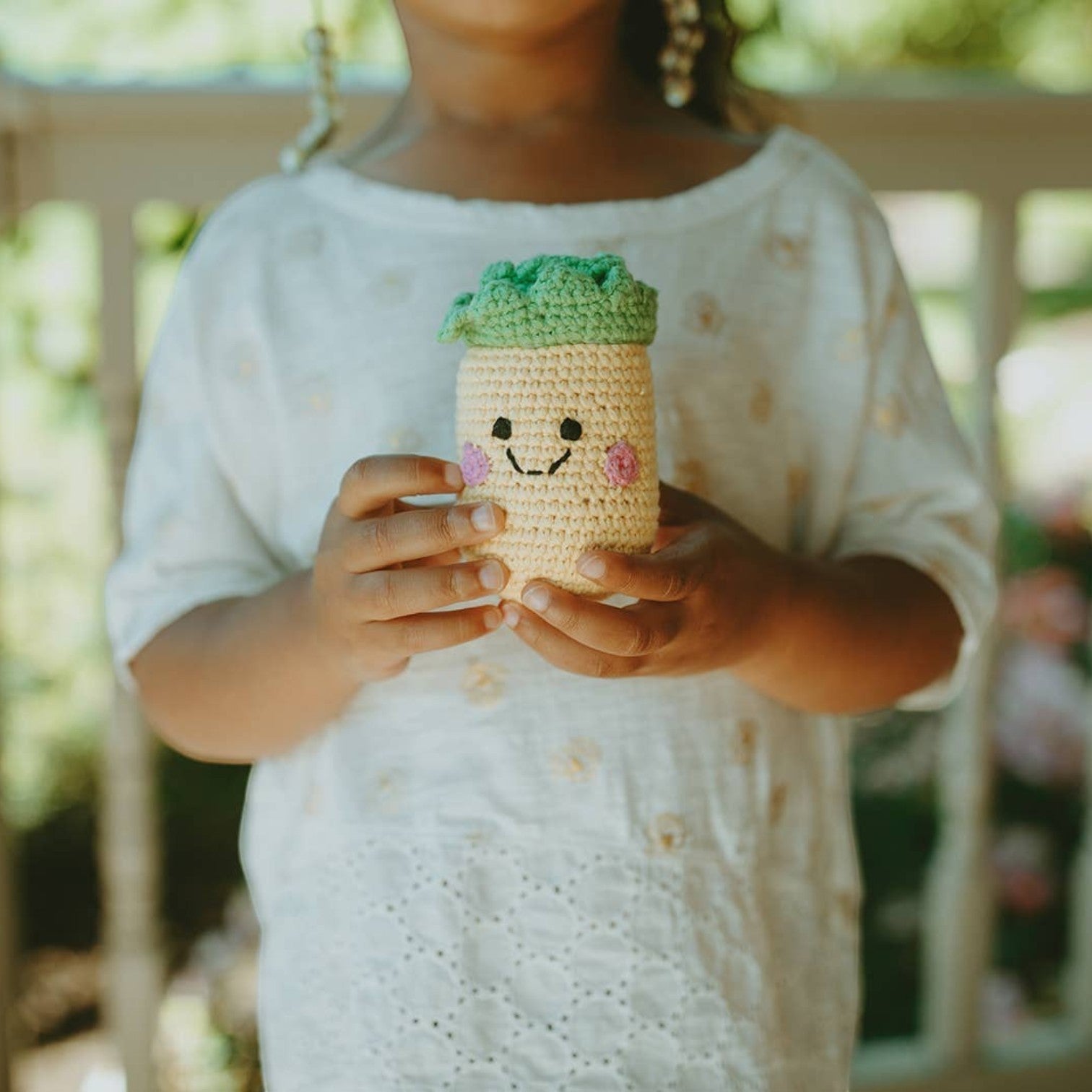 Precious Days Gifts crocheted pineapple rattle toy with a smiling face and green top. Made from 100% cotton.