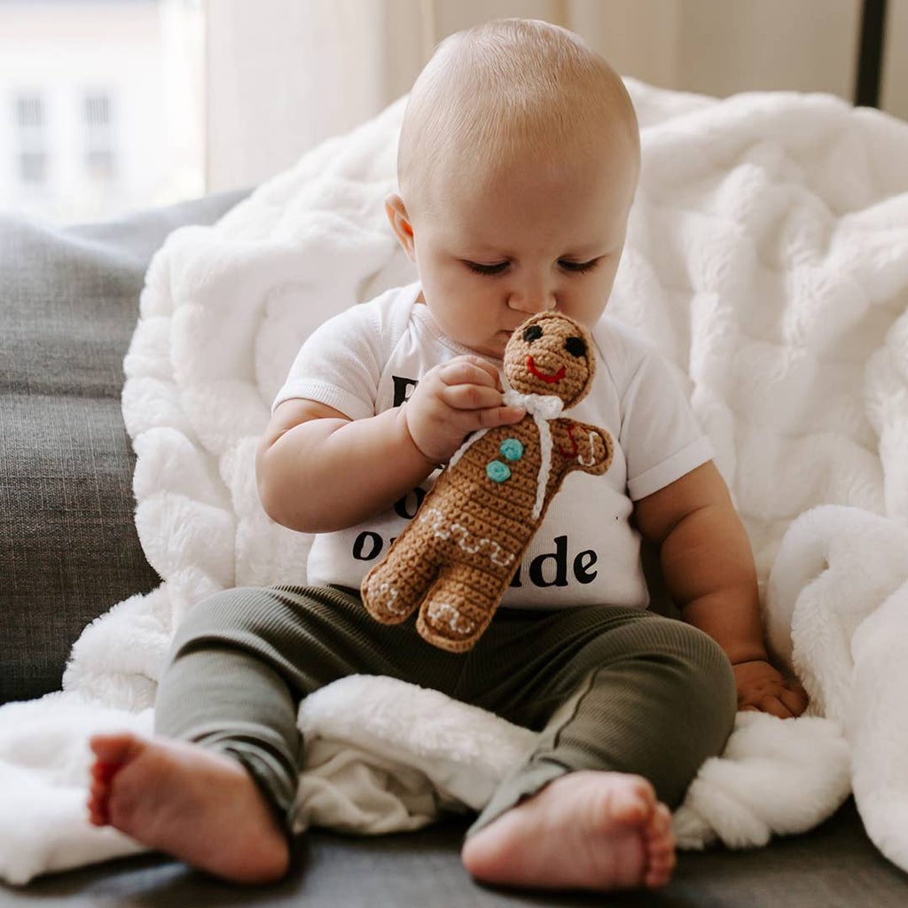 Precious Days Gifts handmade gingerbread man crochet rattle held by a baby sitting on a soft white blanket
