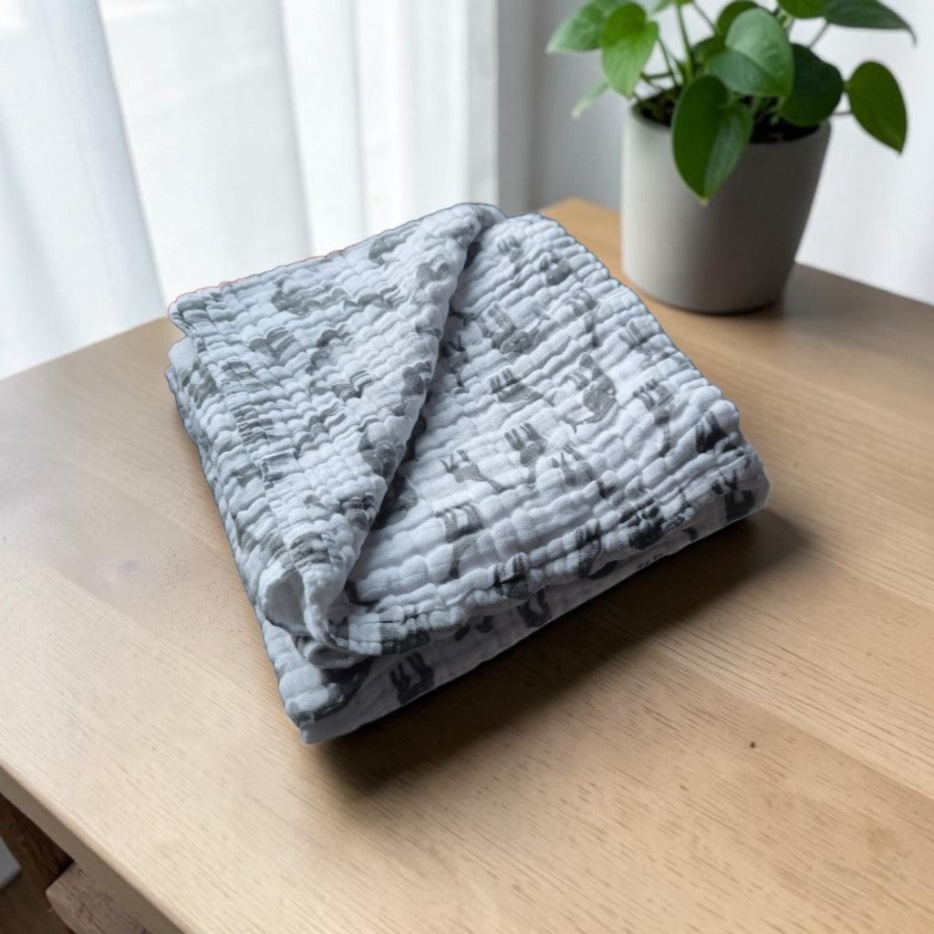 Precious Days Gifts 6-layer muslin baby blanket with a grey giraffe print, folded on a wooden table.