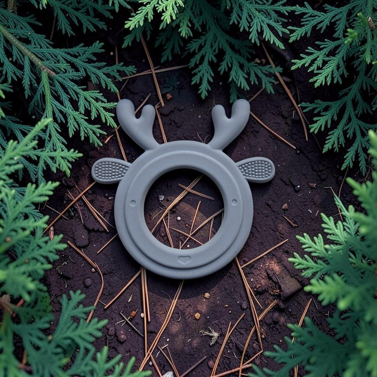 Precious Days Gifts grey silicone reindeer teether with textured surfaces for soothing baby gums on a forest floor