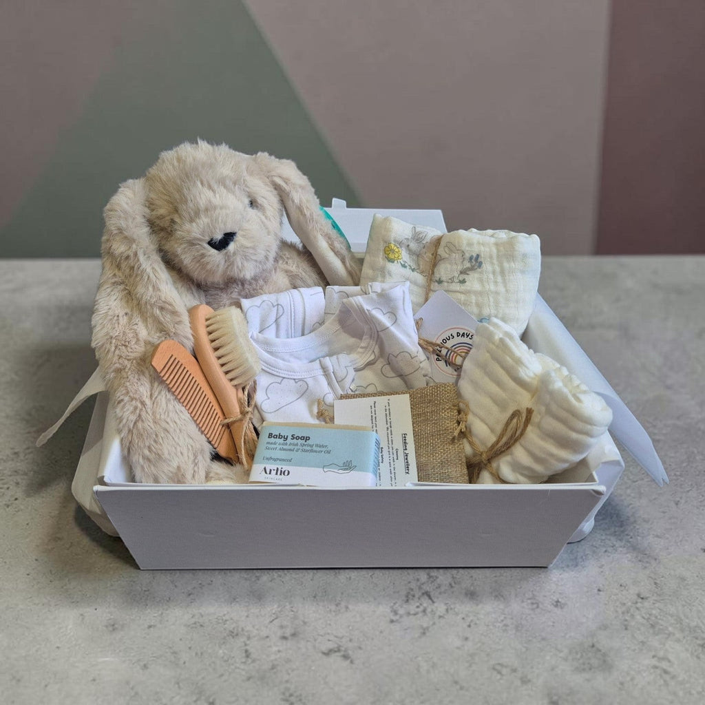 Precious Days Gifts luxury new baby gift box containing a plush bunny toy, cloud onesie, muslin cloths, and baby care items