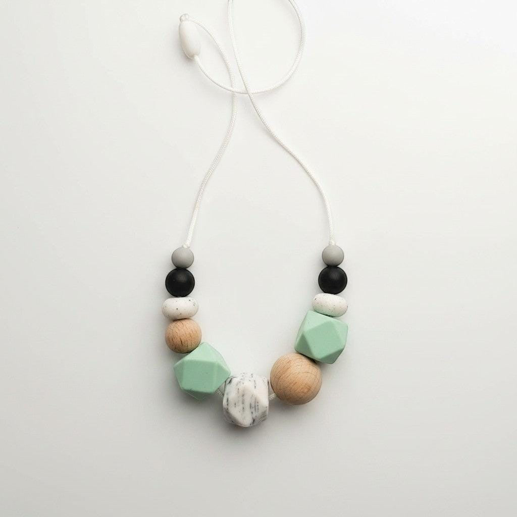 Precious Days Gifts mint green silicone and wood teething necklace with grey, black, and speckled beads.
