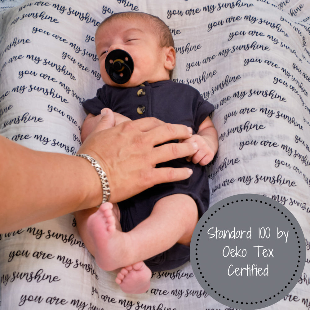 Precious Days Gifts baby swaddled in a You Are My Sunshine cotton muslin blanket with a black pacifier