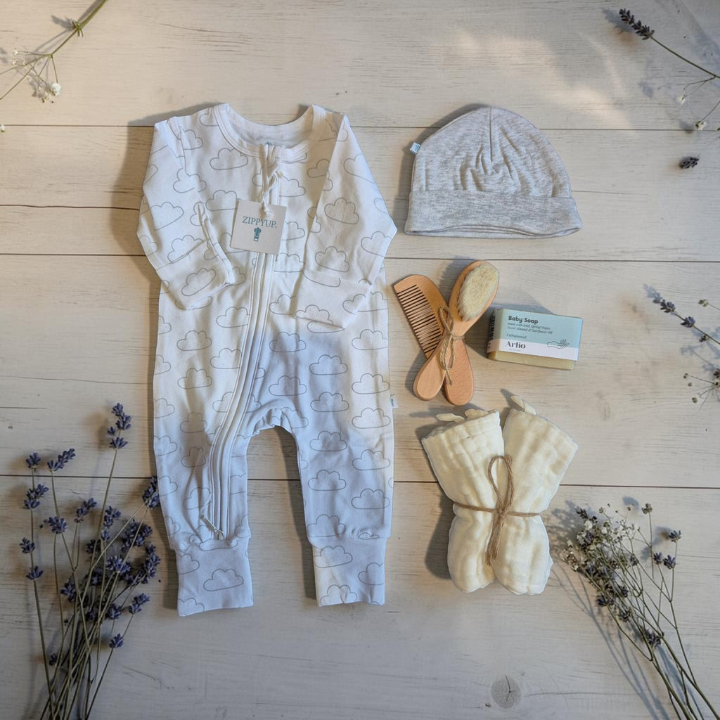 Precious Days Gifts new baby essentials box featuring a cloud print onesie, hat, natural soap, washcloths, and brush.