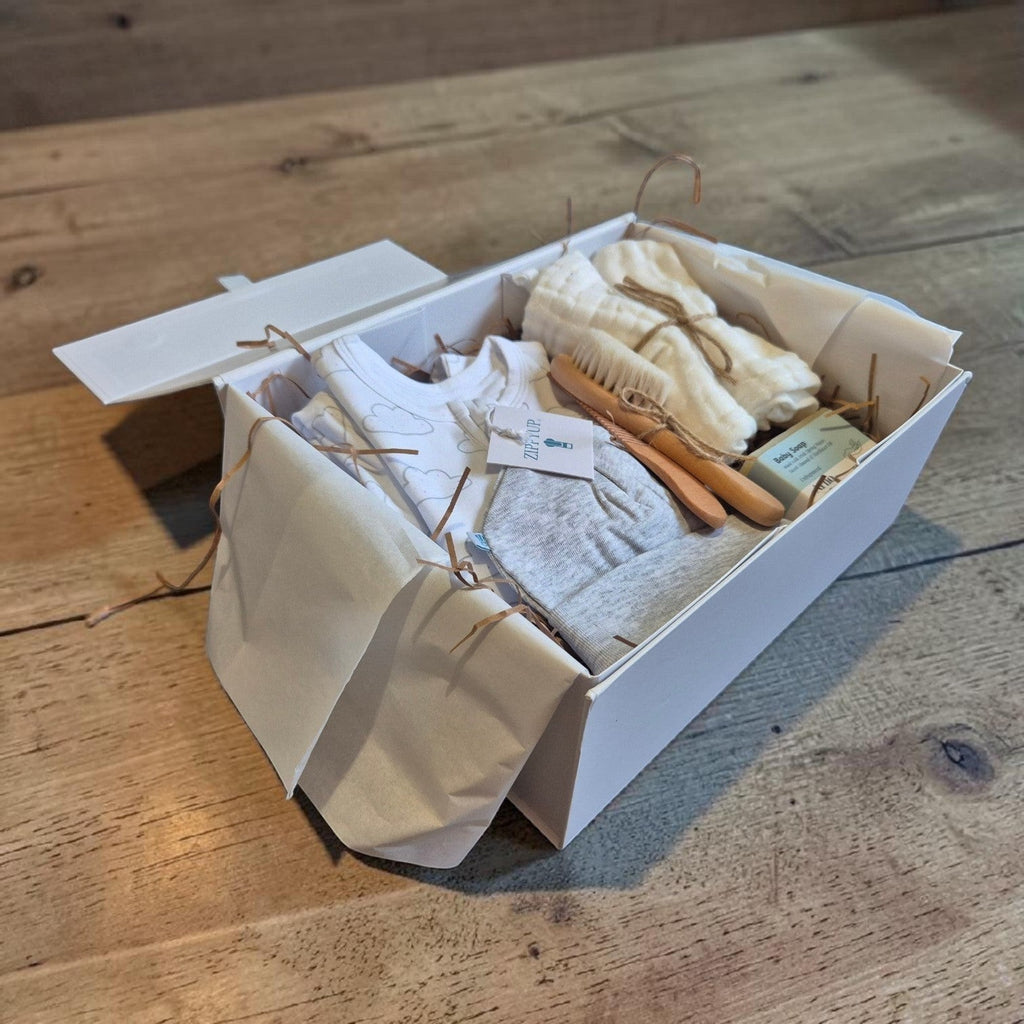 Precious Days Gifts new baby essentials box containing a cloud-patterned onesie, hat, natural soap, and grooming set.
