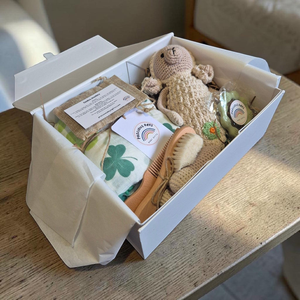 Precious Days Gifts Signature Belfast Box containing a shamrock muslin, crochet sheep rattle, and baby grooming set.