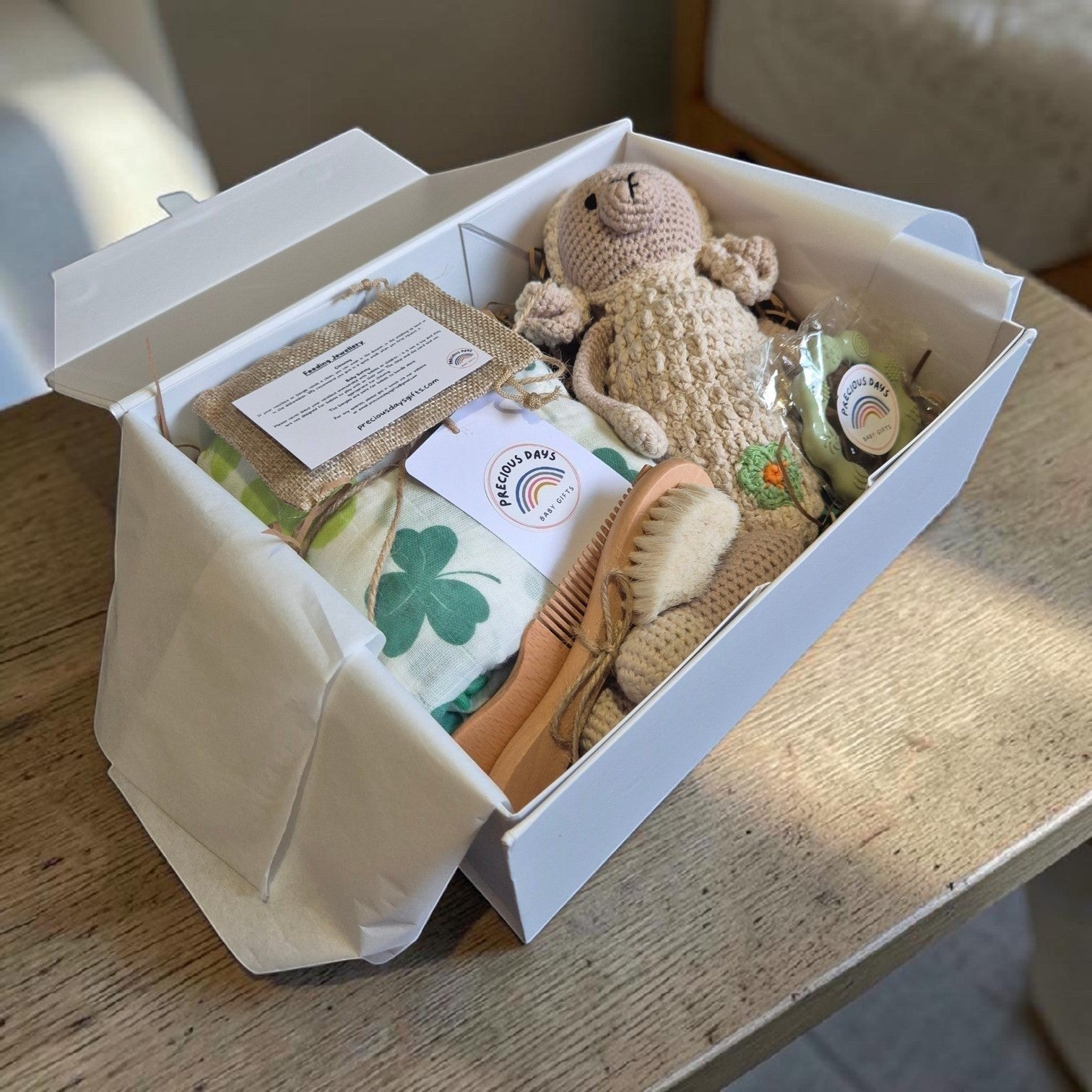 Precious Days Gifts Signature Belfast Box containing a shamrock muslin, crochet sheep rattle, and baby grooming set.