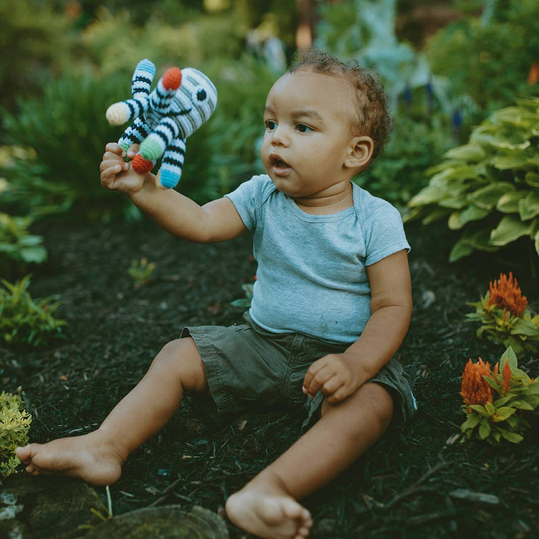 Precious Days Gifts handmade cotton octopus rattle held by a baby sitting in a lush garden setting