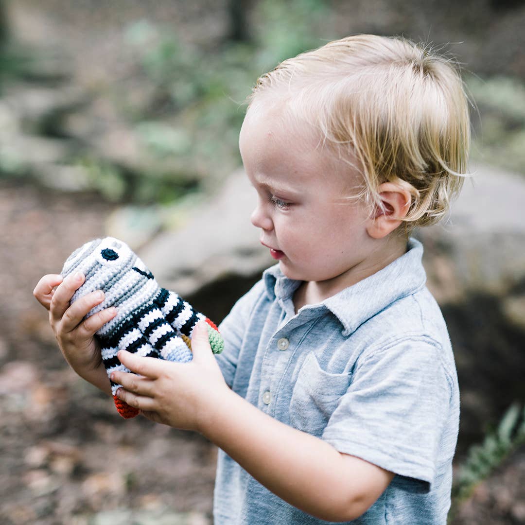 A toddler holding a Precious Days Gifts handmade black and white striped octopus rattle toy in an outdoor setting.