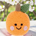 Precious Days Gifts handmade orange crochet baby rattle with a smiling face, green leaf, and brown stem.