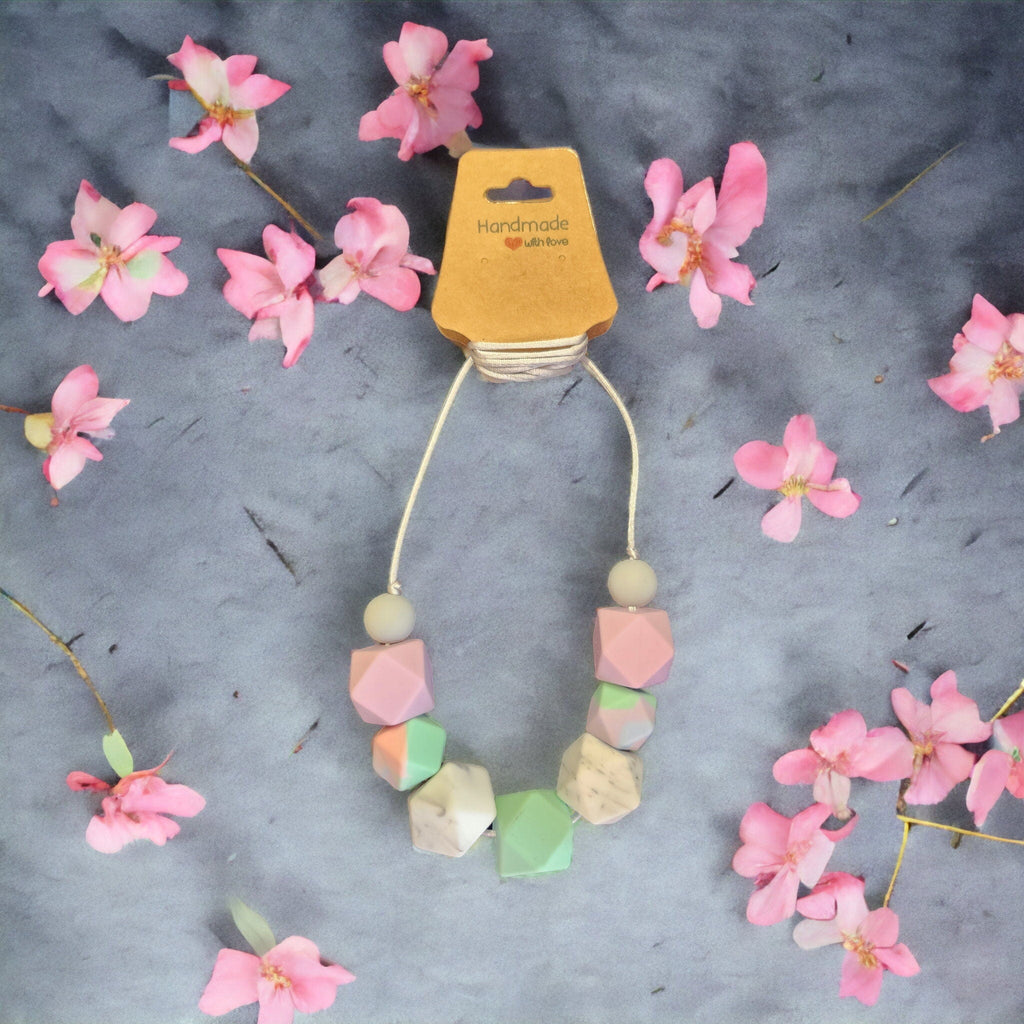 Precious Days Gifts pastel silicone bead breastfeeding necklace on a grey background with pink flower accents
