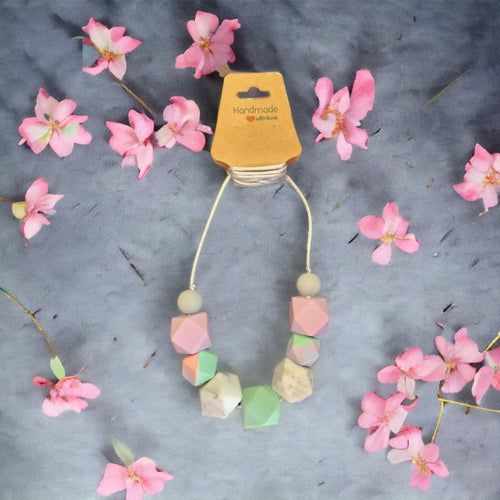 Precious Days Gifts pastel silicone bead breastfeeding necklace on a grey background with pink flower accents