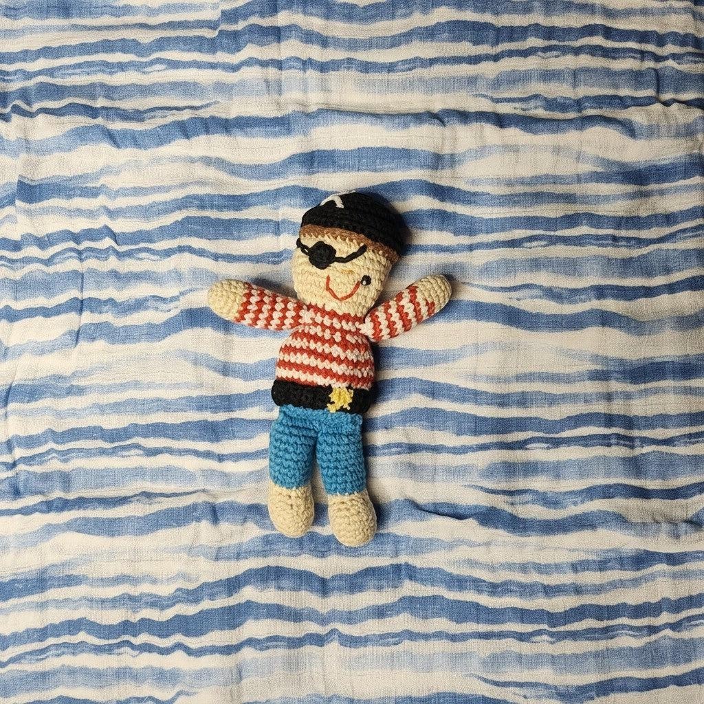 Precious Days Gifts handmade crochet pirate rattle with red striped shirt and blue pants on a blue striped muslin.