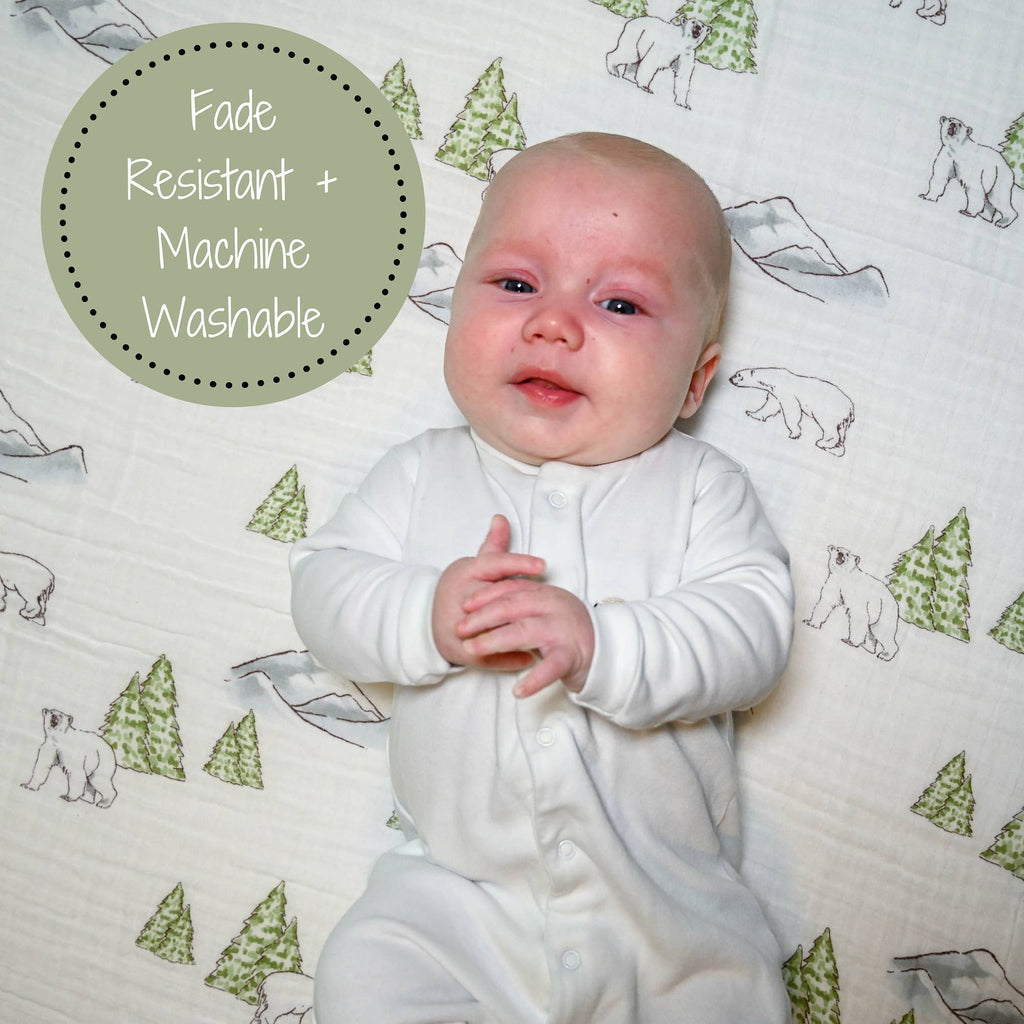 Precious Days Gifts baby lying on a soft cotton muslin swaddle blanket with a polar bear and pine tree print