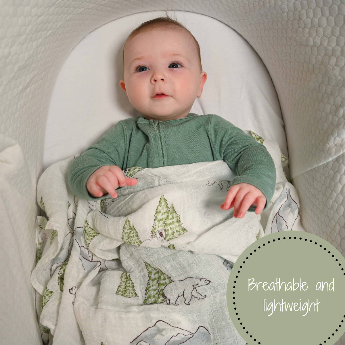 Precious Days Gifts baby swaddle blanket with polar bear and pine tree print in a white bassinet with a baby