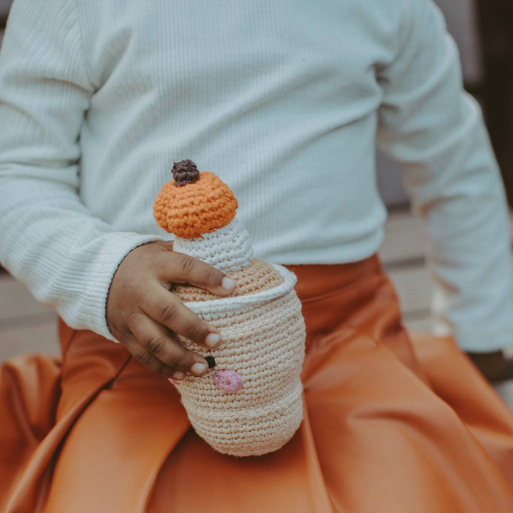 Precious Days Gifts handmade crochet pumpkin spice latte rattle held by a child in a white shirt and orange skirt.