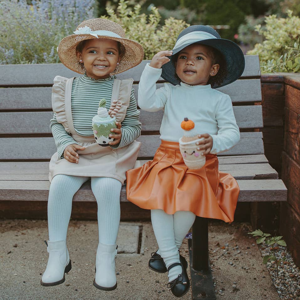 Two toddlers sitting on a park bench holding Precious Days Gifts handmade pumpkin spice latte crochet rattles